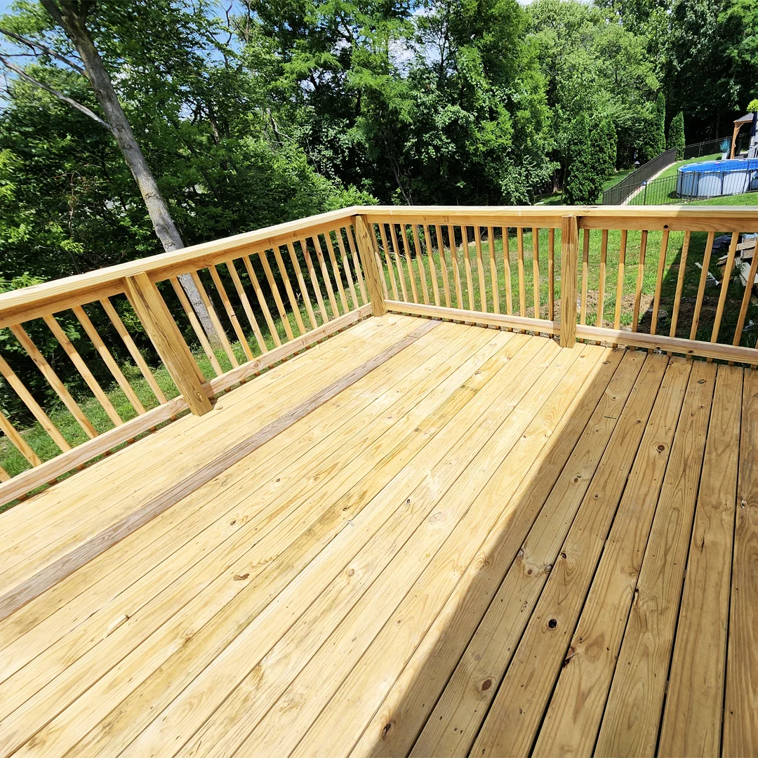 Large new pressure-treated deck with spindle railing overlooking a wooded yard