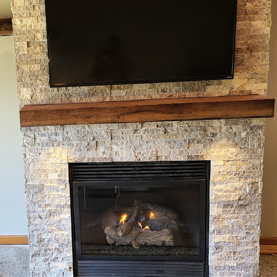 Stacked stone gas fireplace with wood mantel and mounted TV