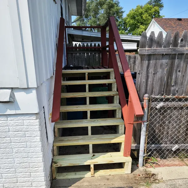 New wooden exterior staircase with painted handrail beside a fence
