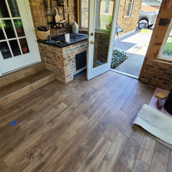 Wood-look flooring in a sunroom with brick wall and glass door