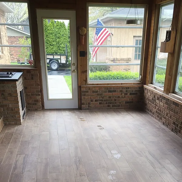 Finished sunroom with brick wall, wood-look flooring and glass door